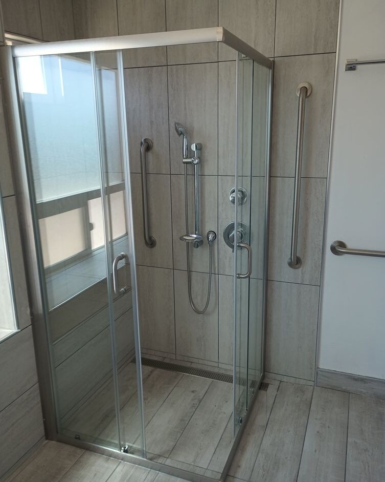 Corner sliding glass shower enclosure with brushed-nickel frame in a tiled bathroom with grab bars