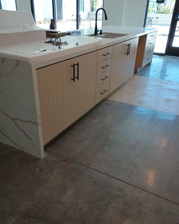 Light wood-grain base cabinets under a waterfall quartz counter with a black faucet, on a concrete floor