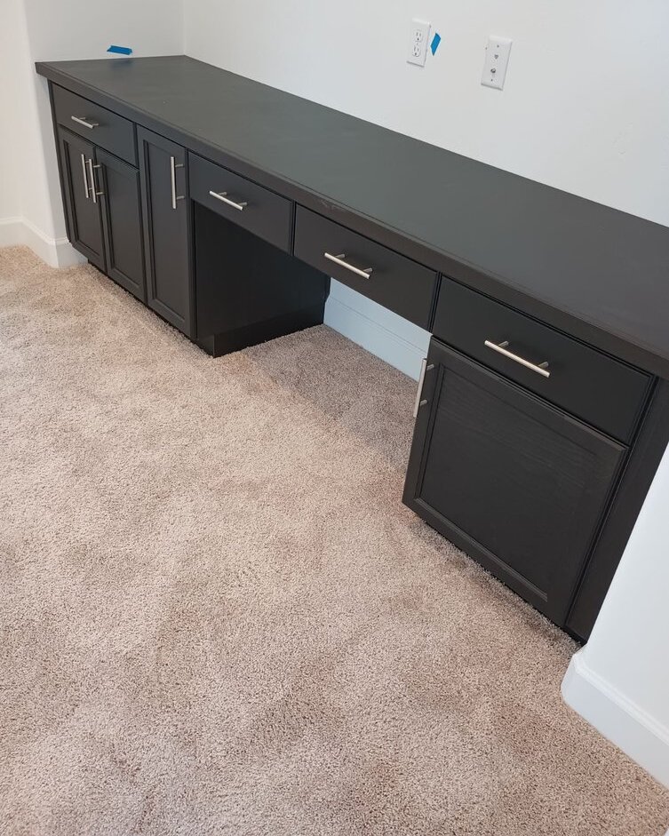 Charcoal built-in desk with drawers and cabinet doors installed along a wall in a carpeted room
