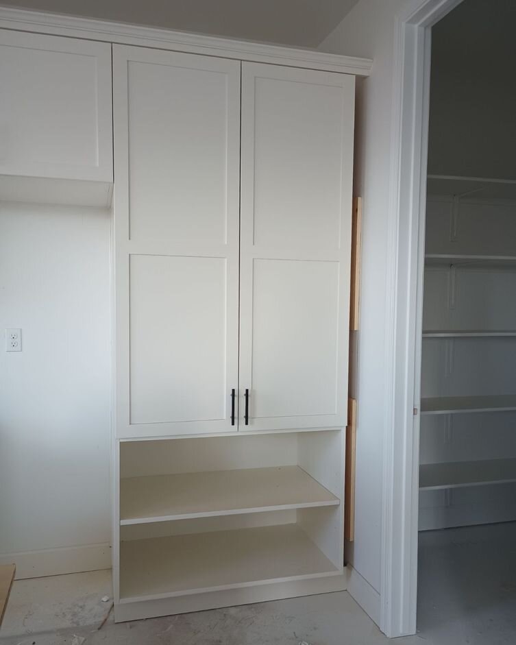 White tall shaker cabinet with black pulls and two open shelves, next to a doorway into a shelved pantry