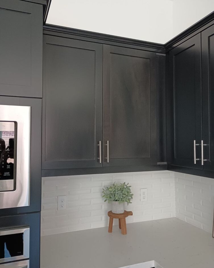 Charcoal upper kitchen cabinets meeting in a corner above a white brick-pattern tile backsplash