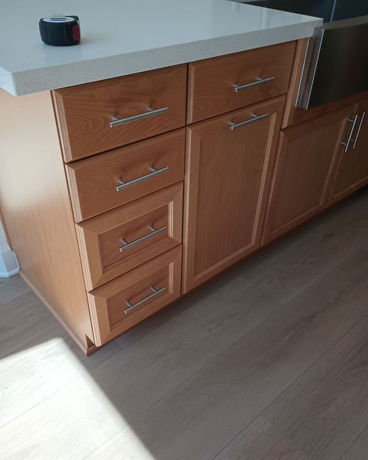 Cherry wood base cabinets with five drawers and bar pulls under a white quartz countertop, a tape measure left on the counter
